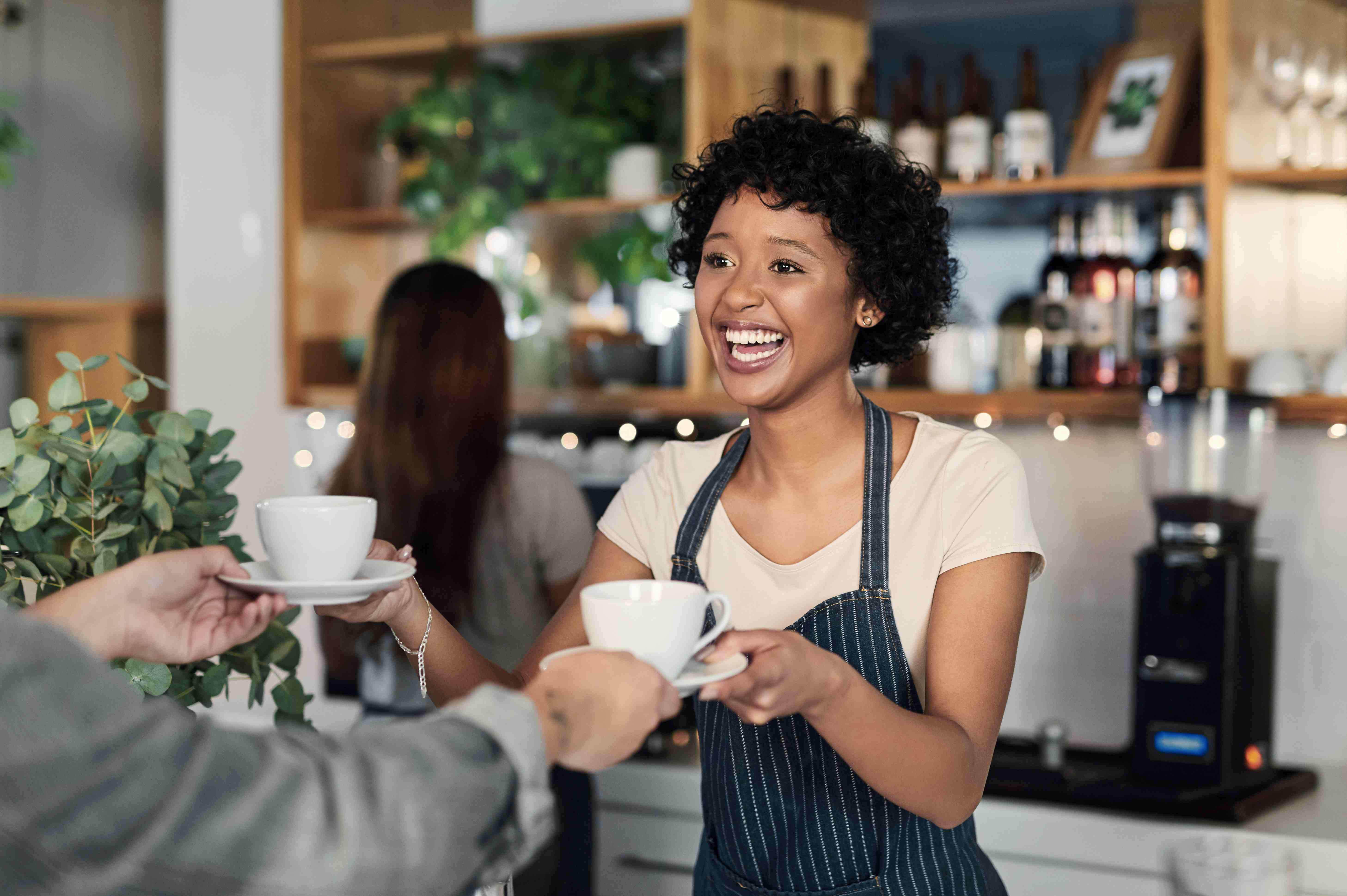 Cafe worker serves customer while small business owner works behind counter.
