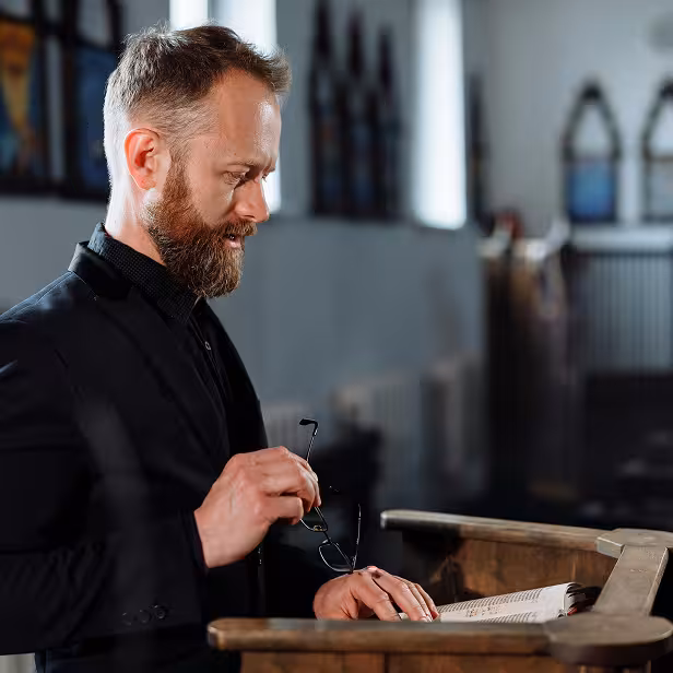 A clergy member stands at a wooden pulpit reading from an open book.