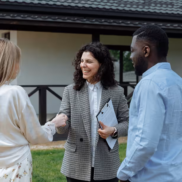 The owner of a small real estate company smiles and shakes hands with a couple who just purchased a home.