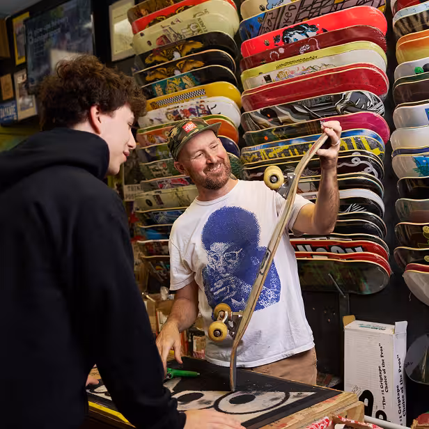 The owner of a skateboard shop shows a skateboard to a customer.