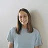 Smiling woman with brown medium-length hair and glasses, wearing a plain light blue T-shirt