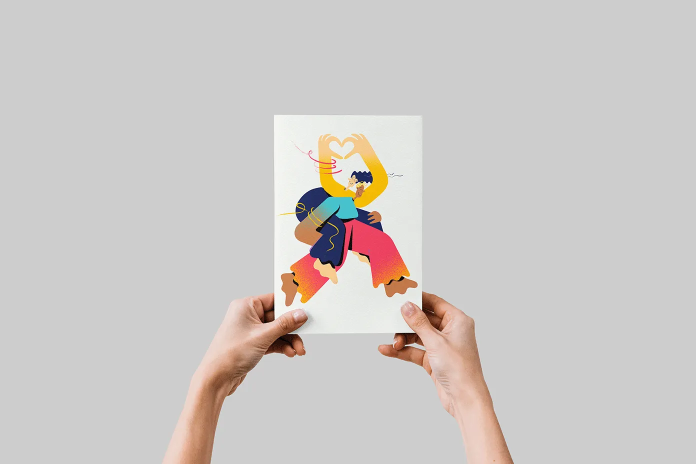 Two hands hold up a sheet of paper with an illustration showing two abstractly colorful illustrated people. One person is carrying the other piggyback and the second person is forming a heart with their hands.