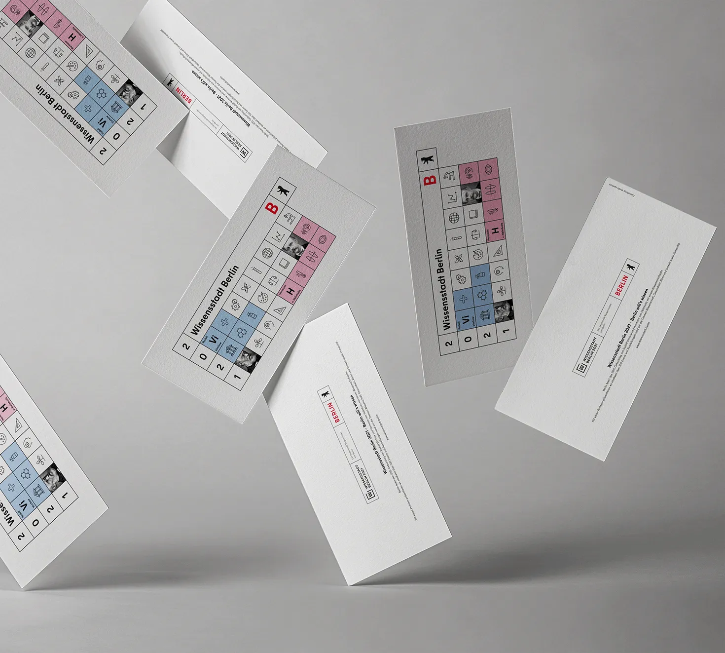 Several falling flyers of the Senate in Berlin with the current theme for the annual card 2021 with the motto " City of Knowledge Berlin". The design is a geometric illustration in the colors white, black, red, light blue and pink, structured like a periodic table filled with various icons on the subject of science.