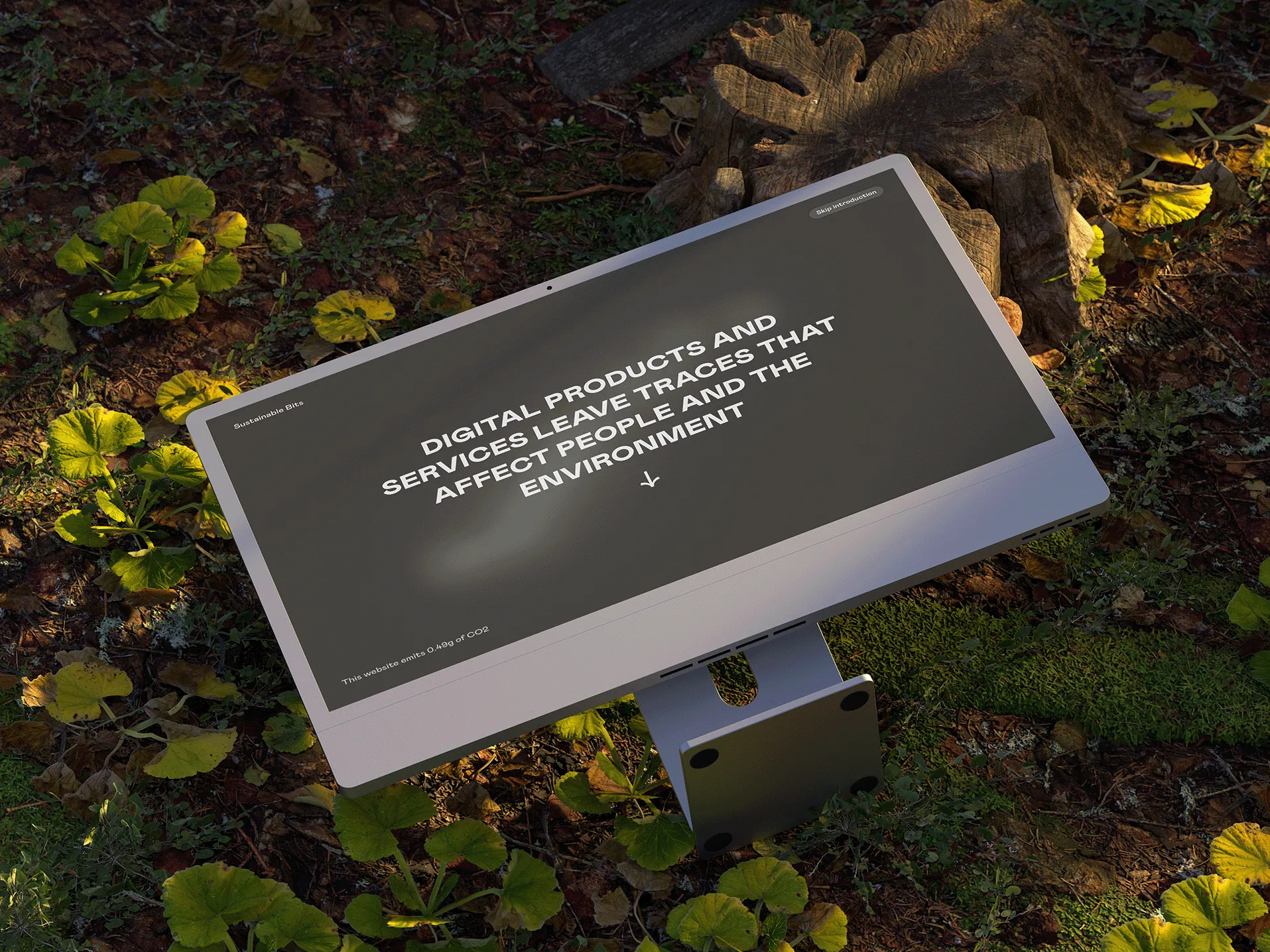 iMac computer lying overturned on a wild and green overgrown surface. The screen shows the introduction to the website "Sustainable Bits" with the sentence "Digital products and services leave traces that affect people and the environment". The mouse also leaves a gray blurred trail as it moves across the screen.