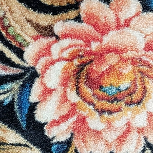 Motif floral rose et orange détaillé sur un tapis texturé avec des accents de bleu et de noir.