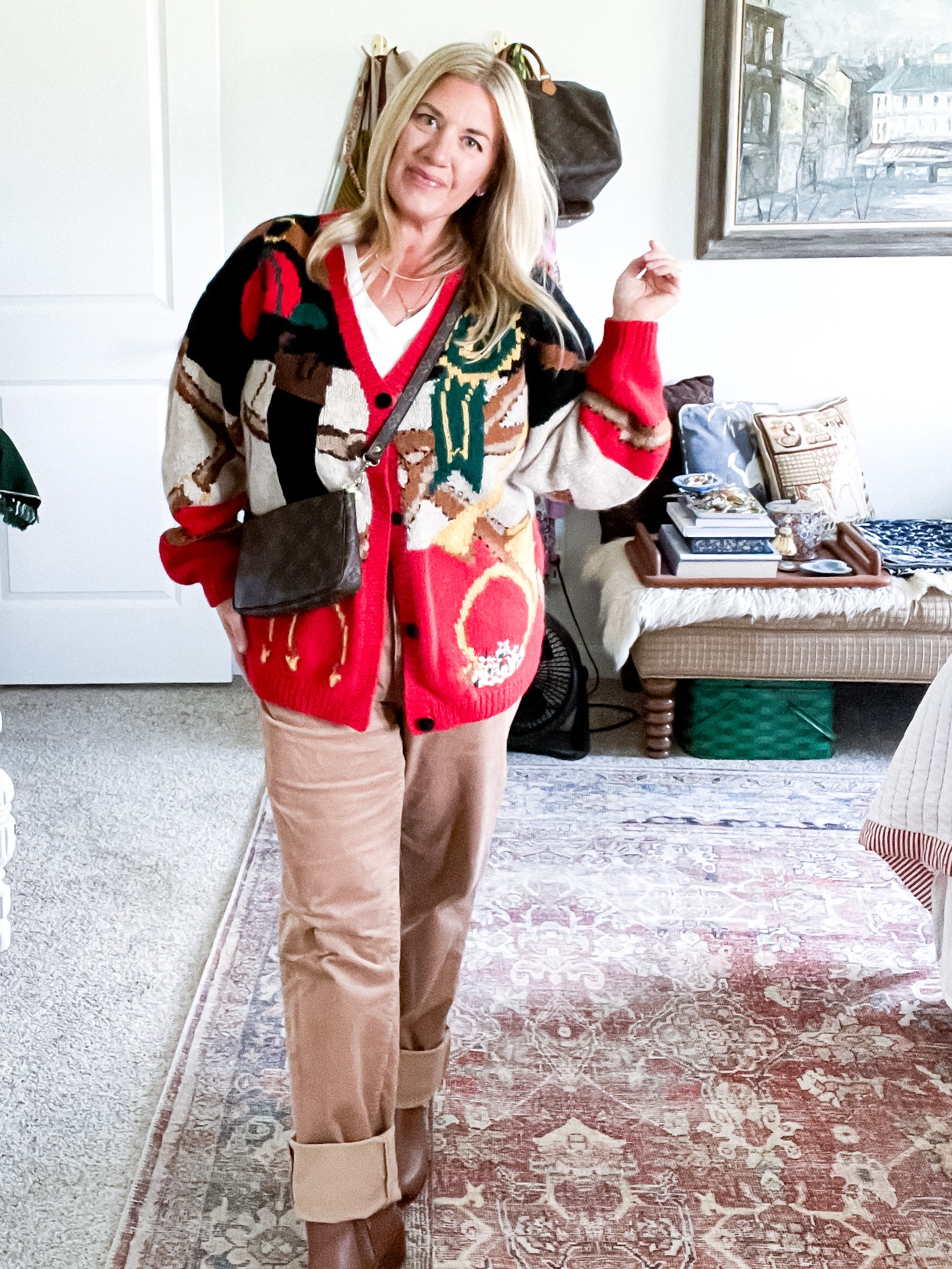 woman in her bedroom wearing a vintage equestrian themed sweater, brown corduroy pants, brown leather booties, and a vintage louis vuitton pochette