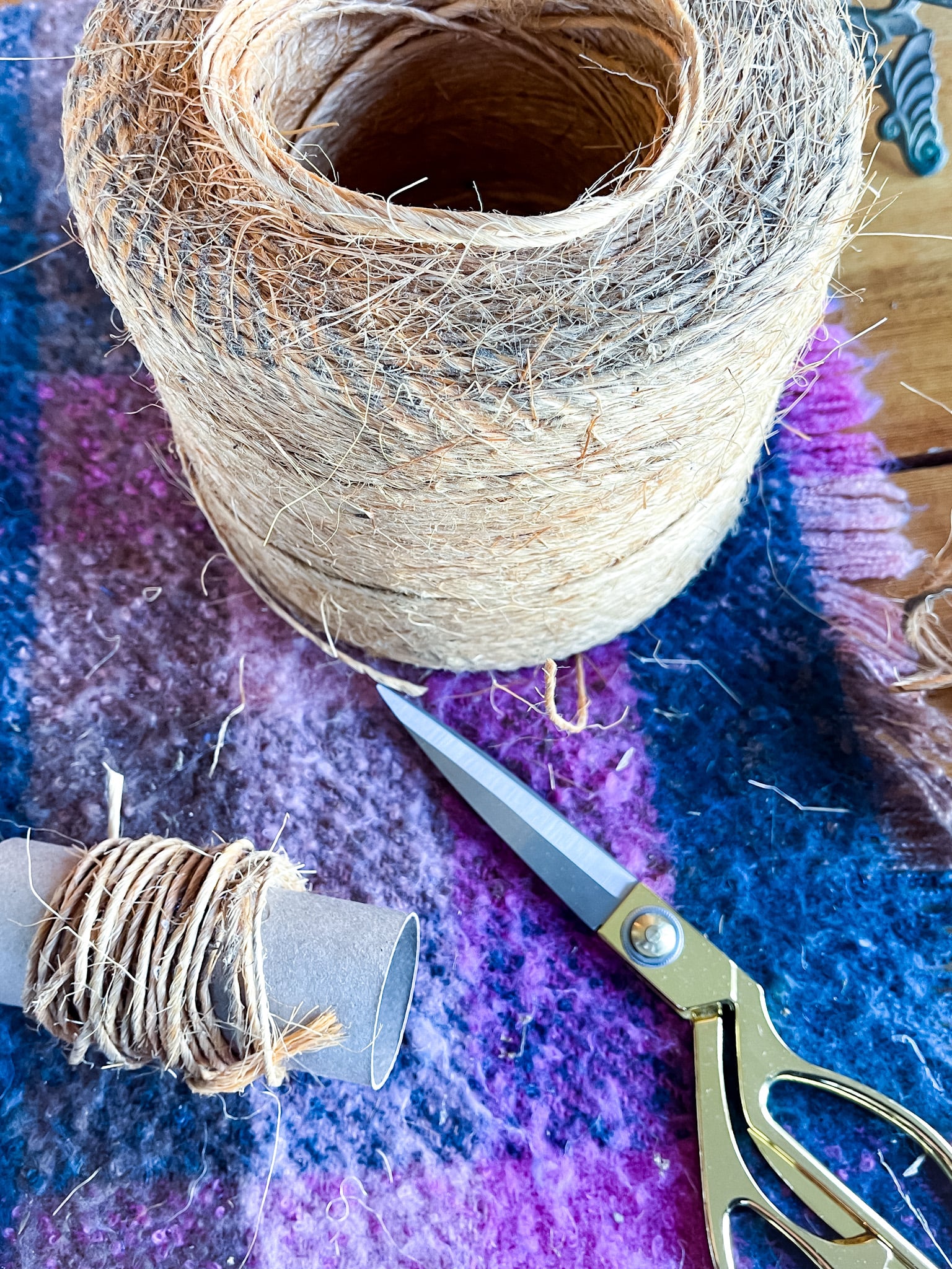 Roll of twine, gold scissors, toilet paper roll wrapped with twine on a table