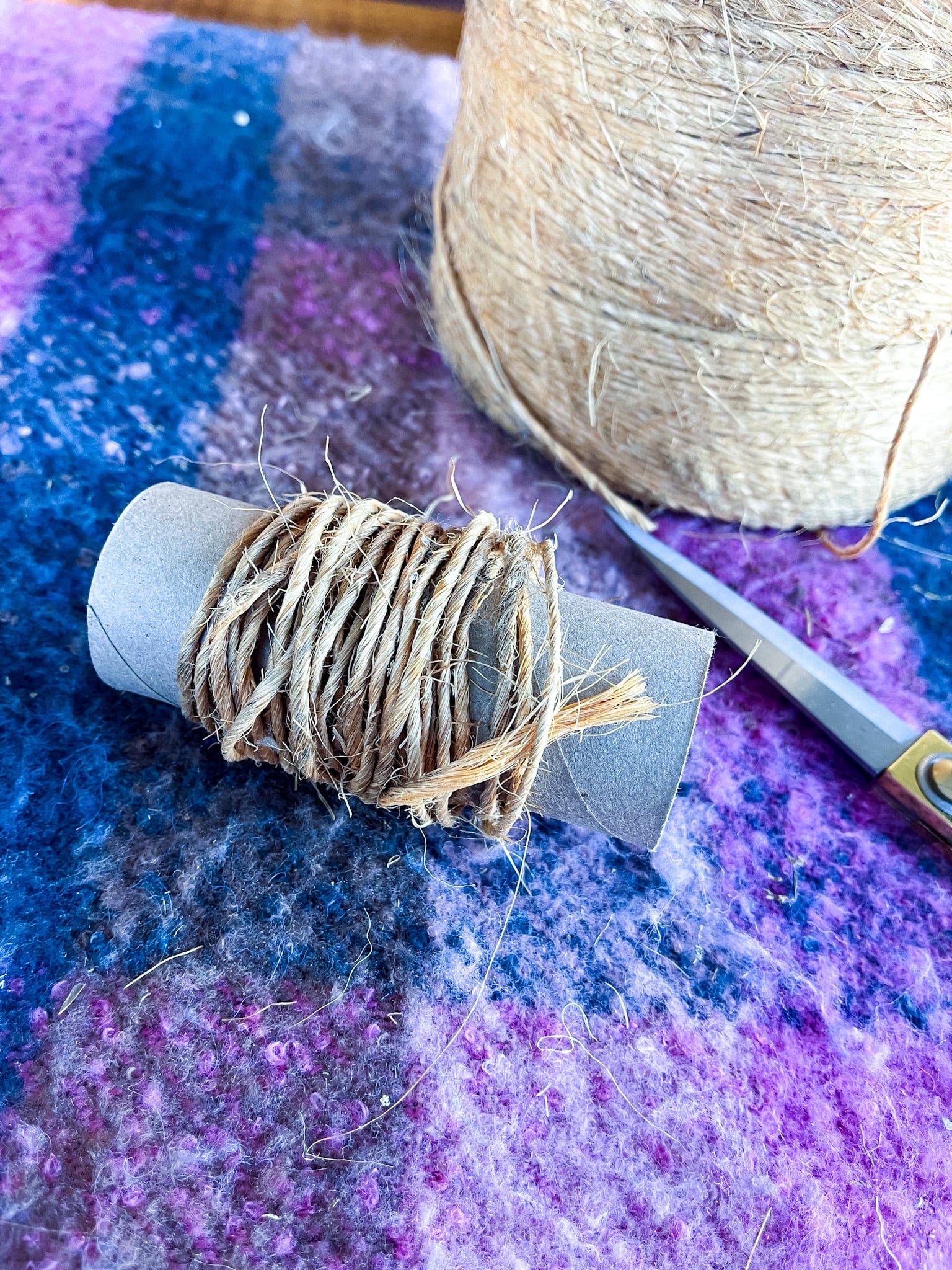 Roll of twine, gold scissors, toilet paper roll wrapped with twine on a table