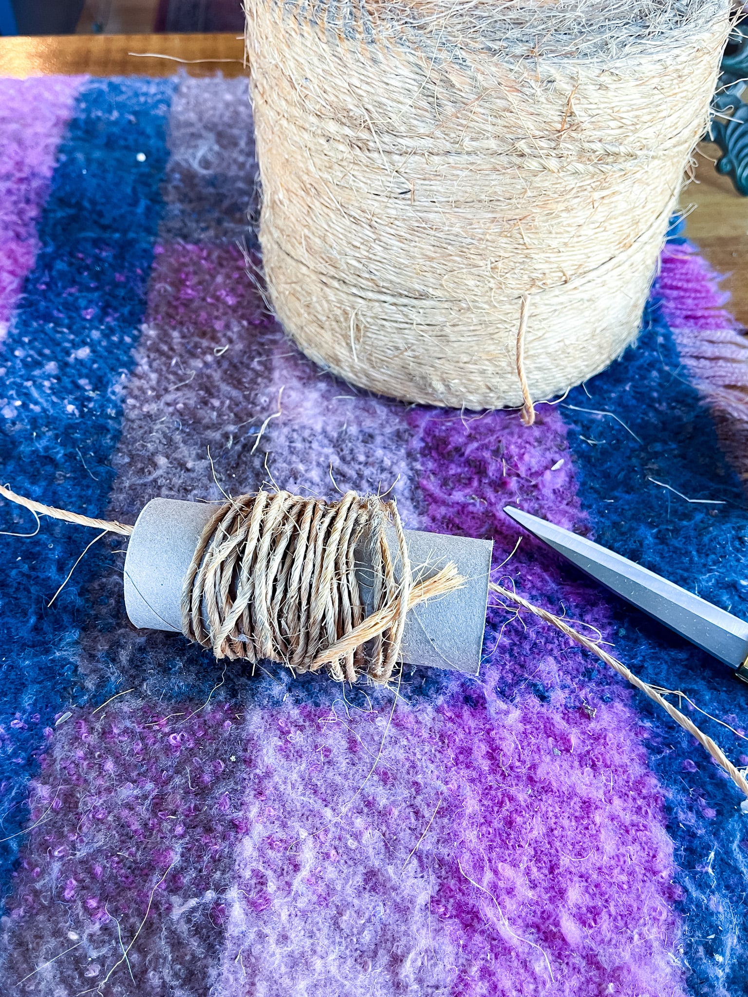 Roll of twine, gold scissors, toilet paper roll wrapped with twine on a table