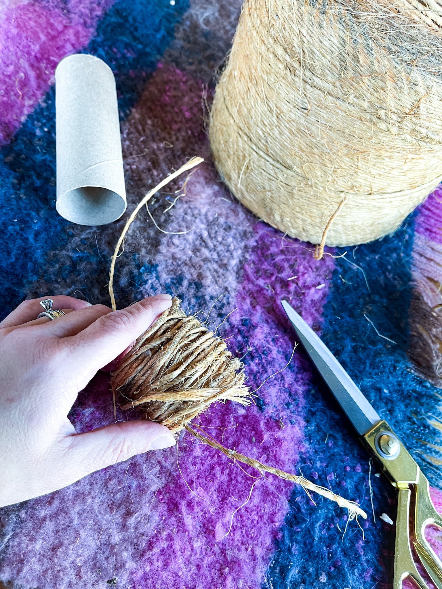 Roll of twine, gold scissors, toilet paper roll wrapped with twine on a table
