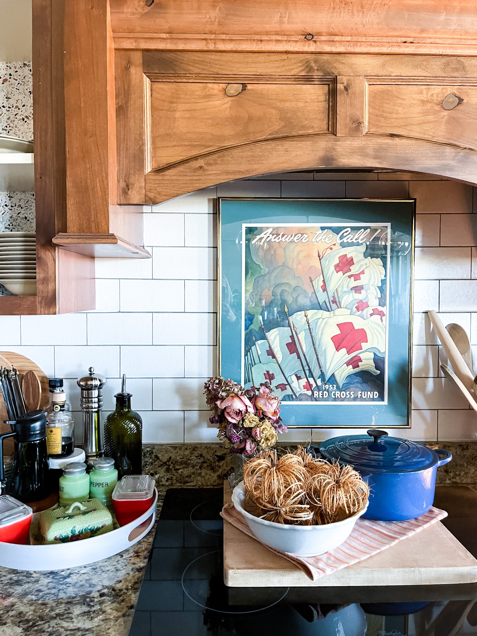 twine pumpkins in an ironstone bowl on a cutting board with a bouquet of dried flowers and a blue le creuset dutch oven