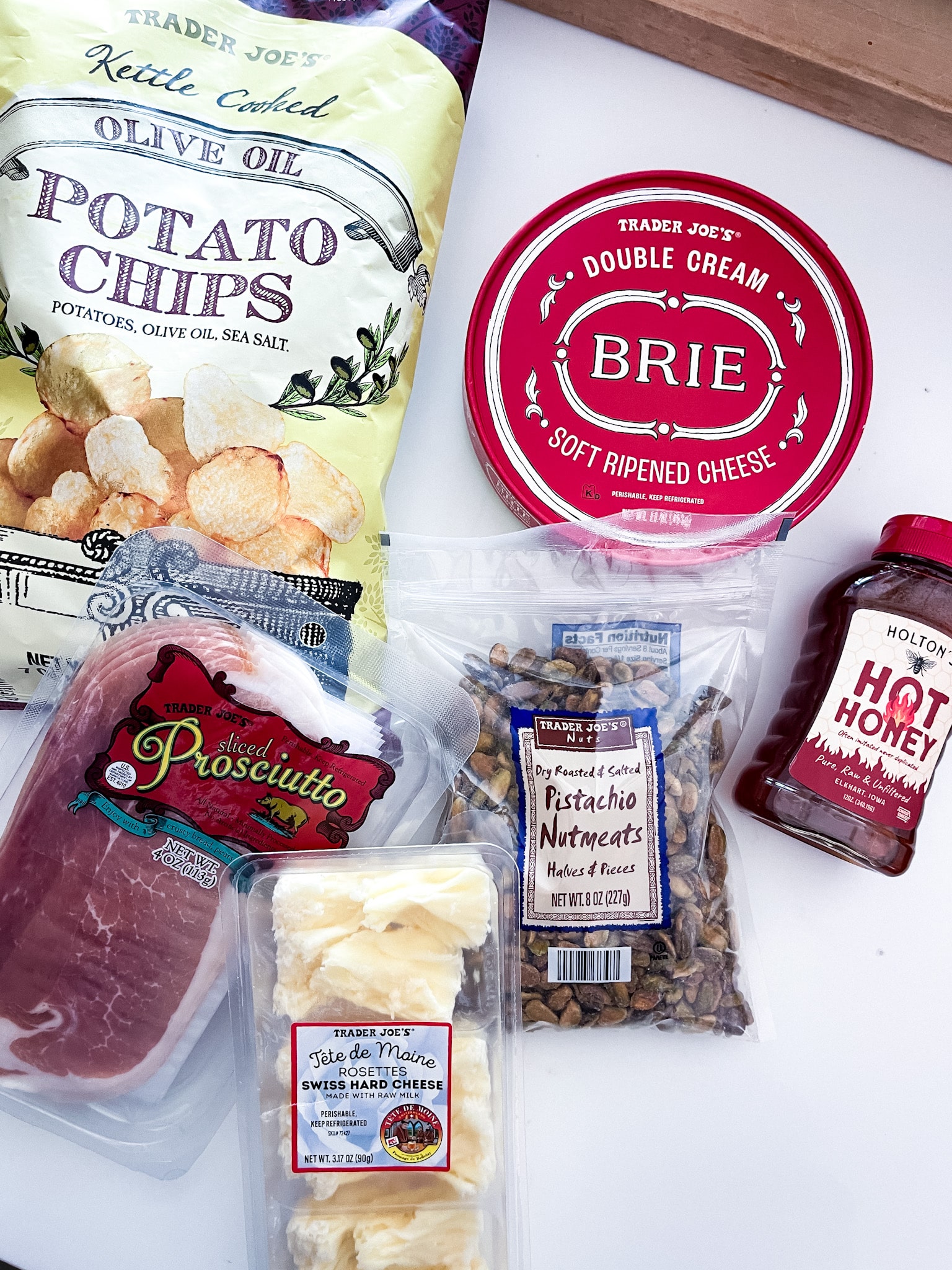 white marble with ingredients from Trader Joe's: potato chips, brie, prosciutto, pistachios, hot honey, tete de moine rosettes