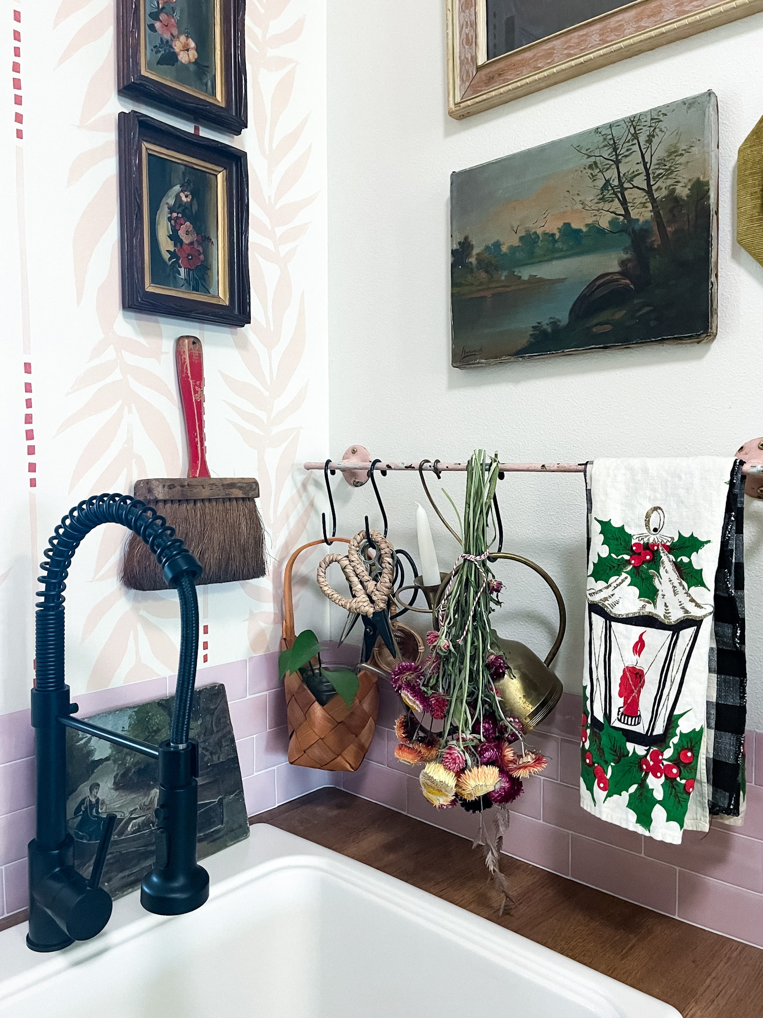 Laundry room utility sink with pink wallpaper behind it, a pink towel bar, vintage art, and a Christmas towel
