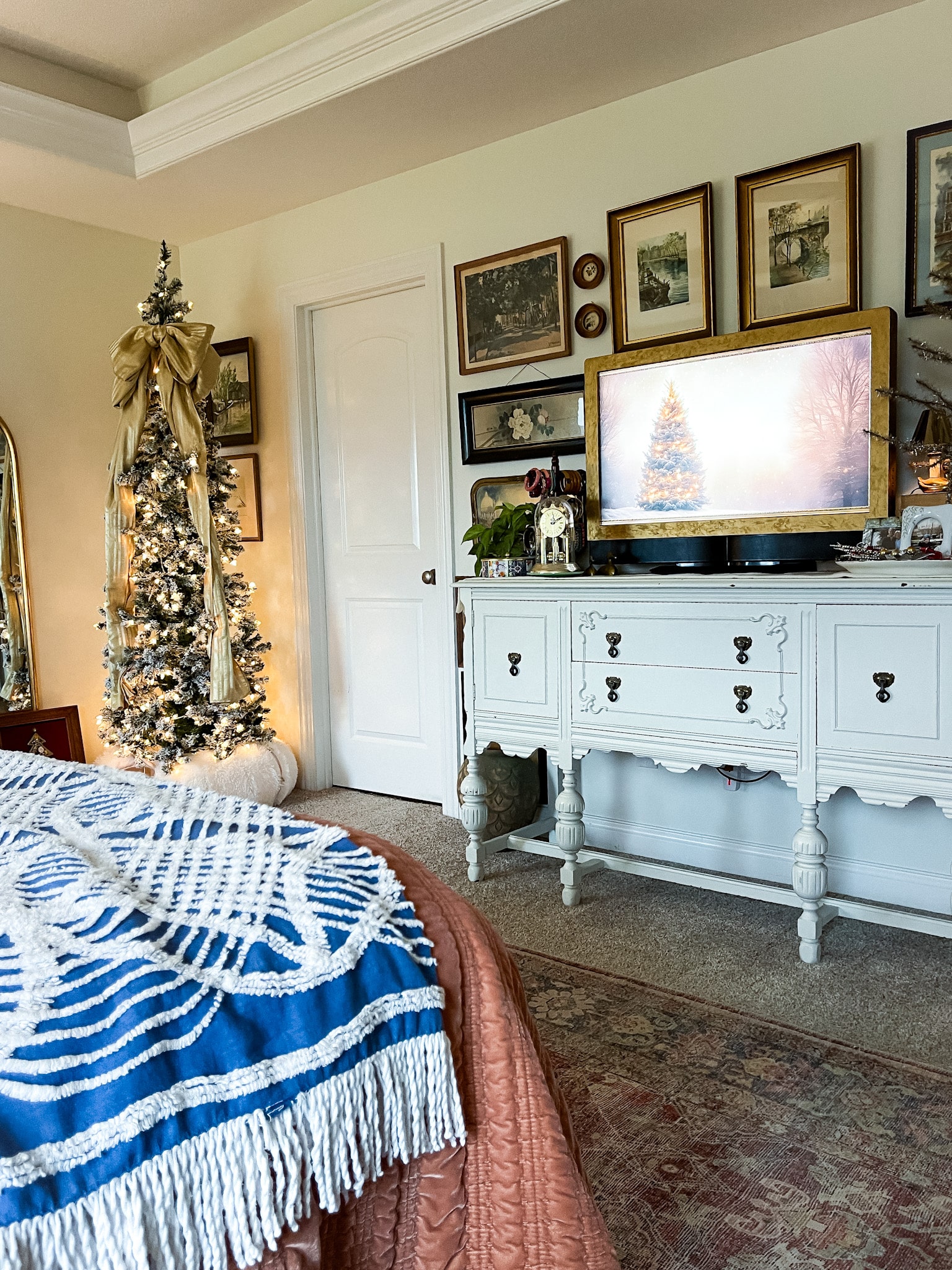 Bedroom with a flocked pencil tree in the corner and a buffet with a tv on it surrounded by a gallery wall