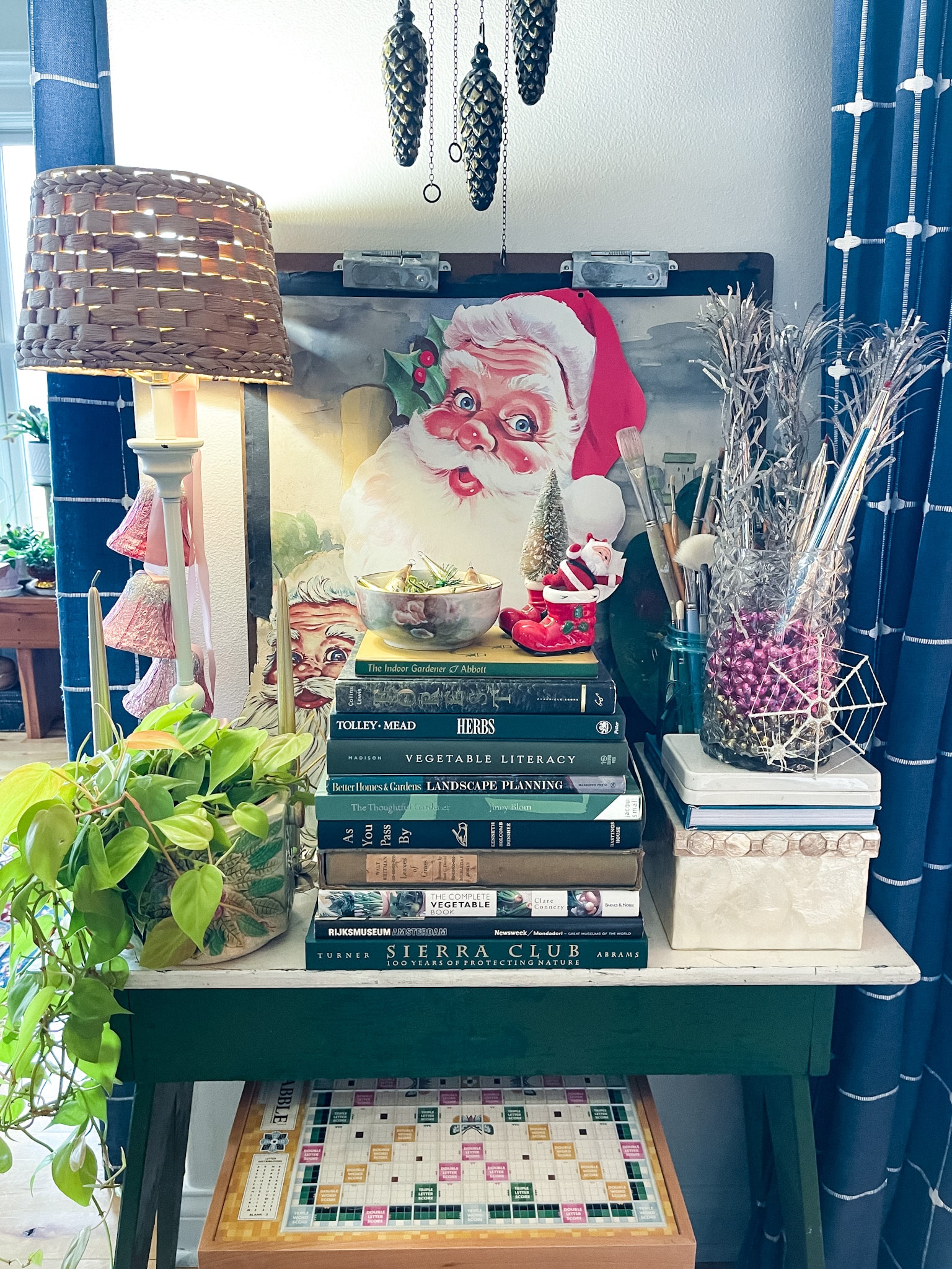green chippy table with a stack of gardening books, art supplies, a lamp and plant, and vintage Christmas decor