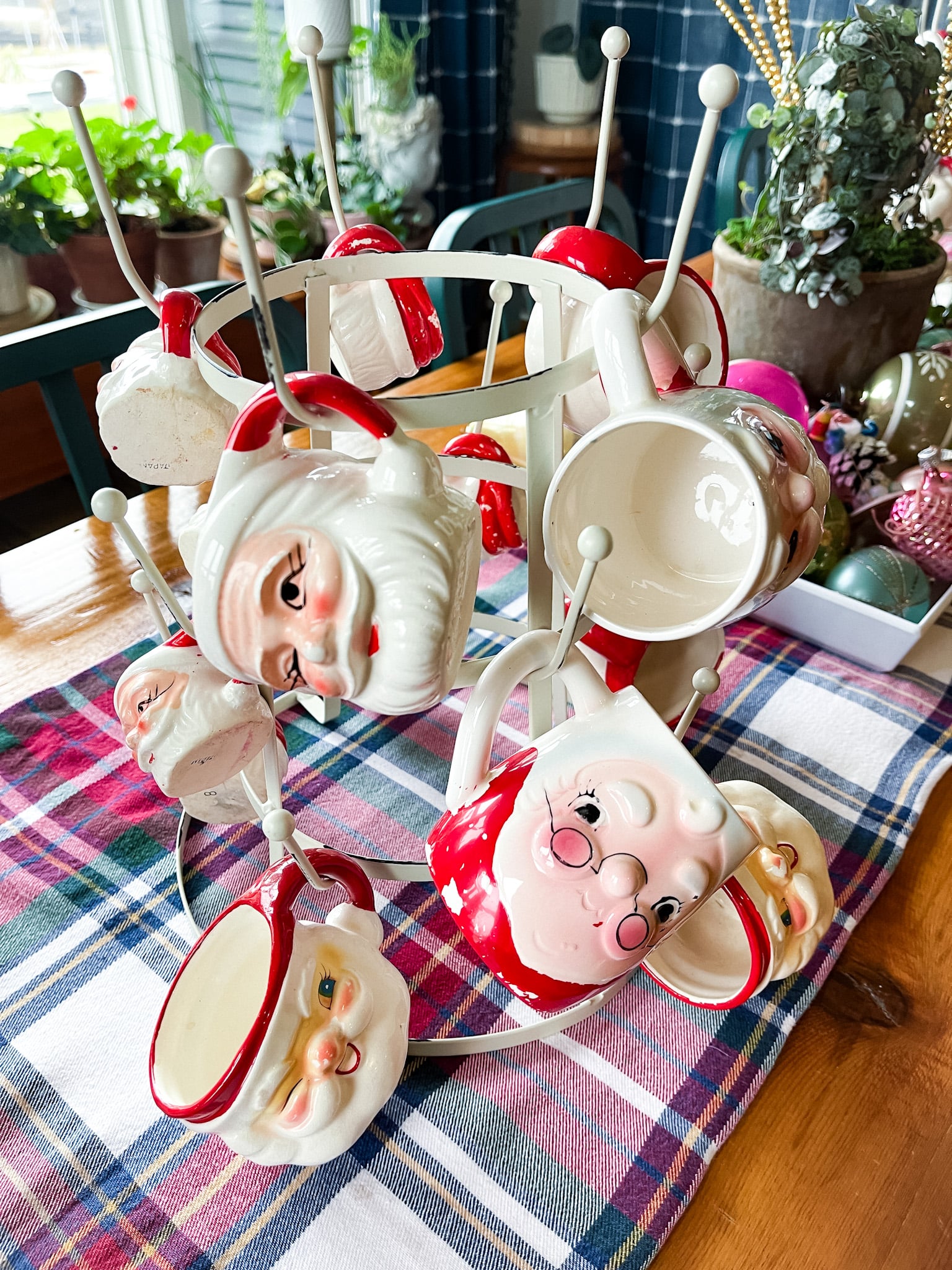 farmhouse table filled with vintage christmas decorations, including santa mugs