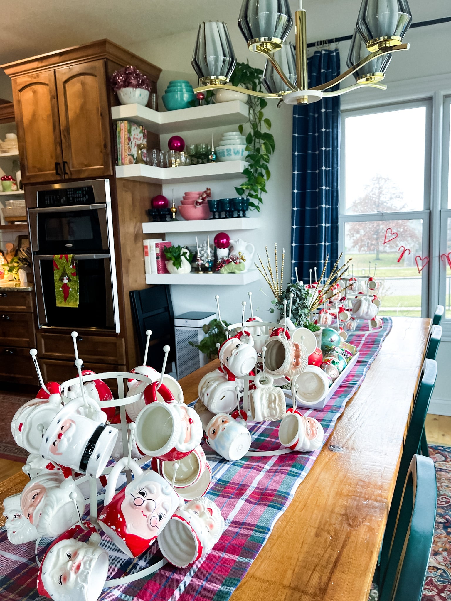farmhouse table filled with vintage christmas decorations, including santa mugs. floating shelves in the background filled with vintage dishes 