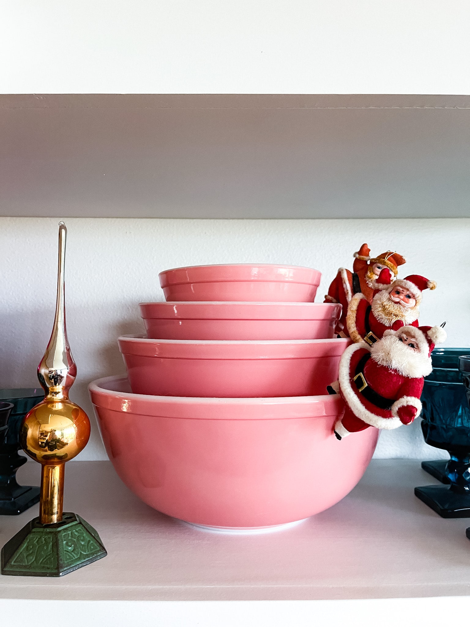 floating shelves with nesting pink pyrex bowls, dancing santas, and shiny brite tree topper