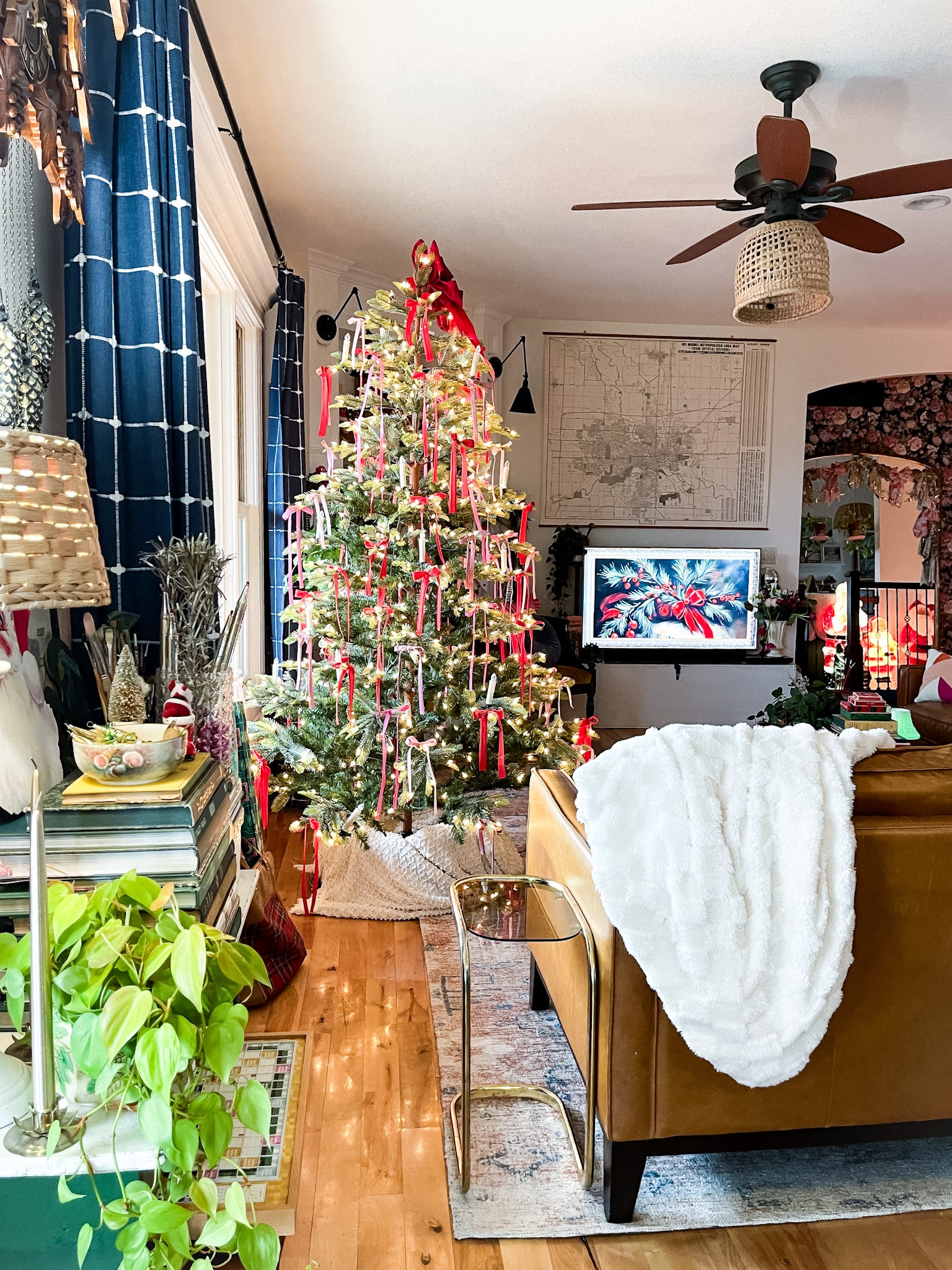 view into a living room with blue plaid curtains, a christmas tree with pink and red ribbons, leather couch, and an art tv