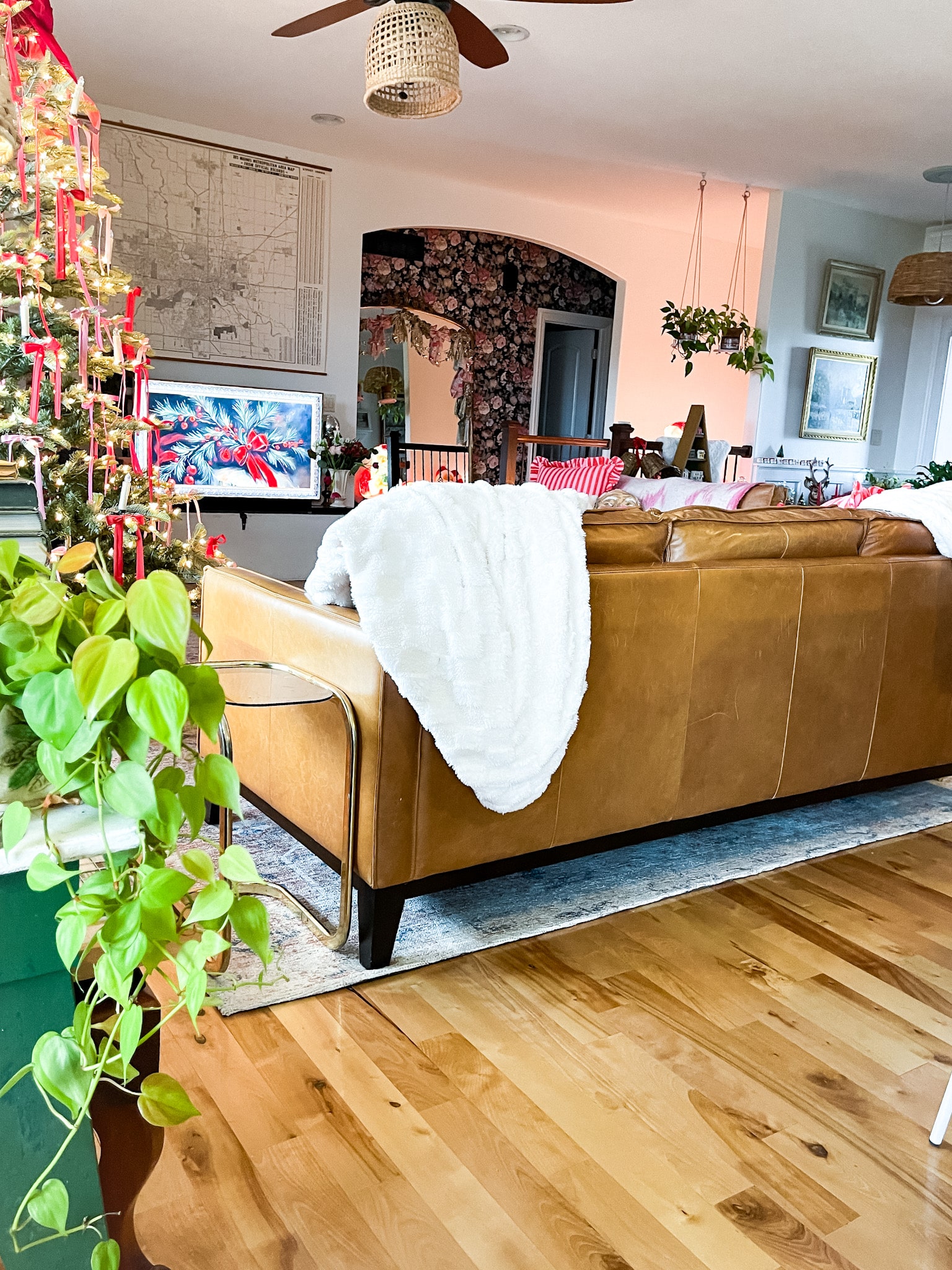 view into a living room with blue plaid curtains, a christmas tree with pink and red ribbons, leather couch, and an art tv