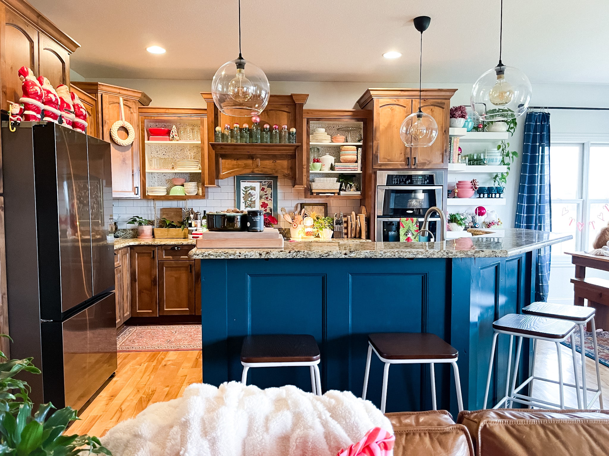 kitchen with medium wood cabinets, a blue painted island, open shelving, and three globe pendant lights. Bits of vintage Christmas scattered throughout.