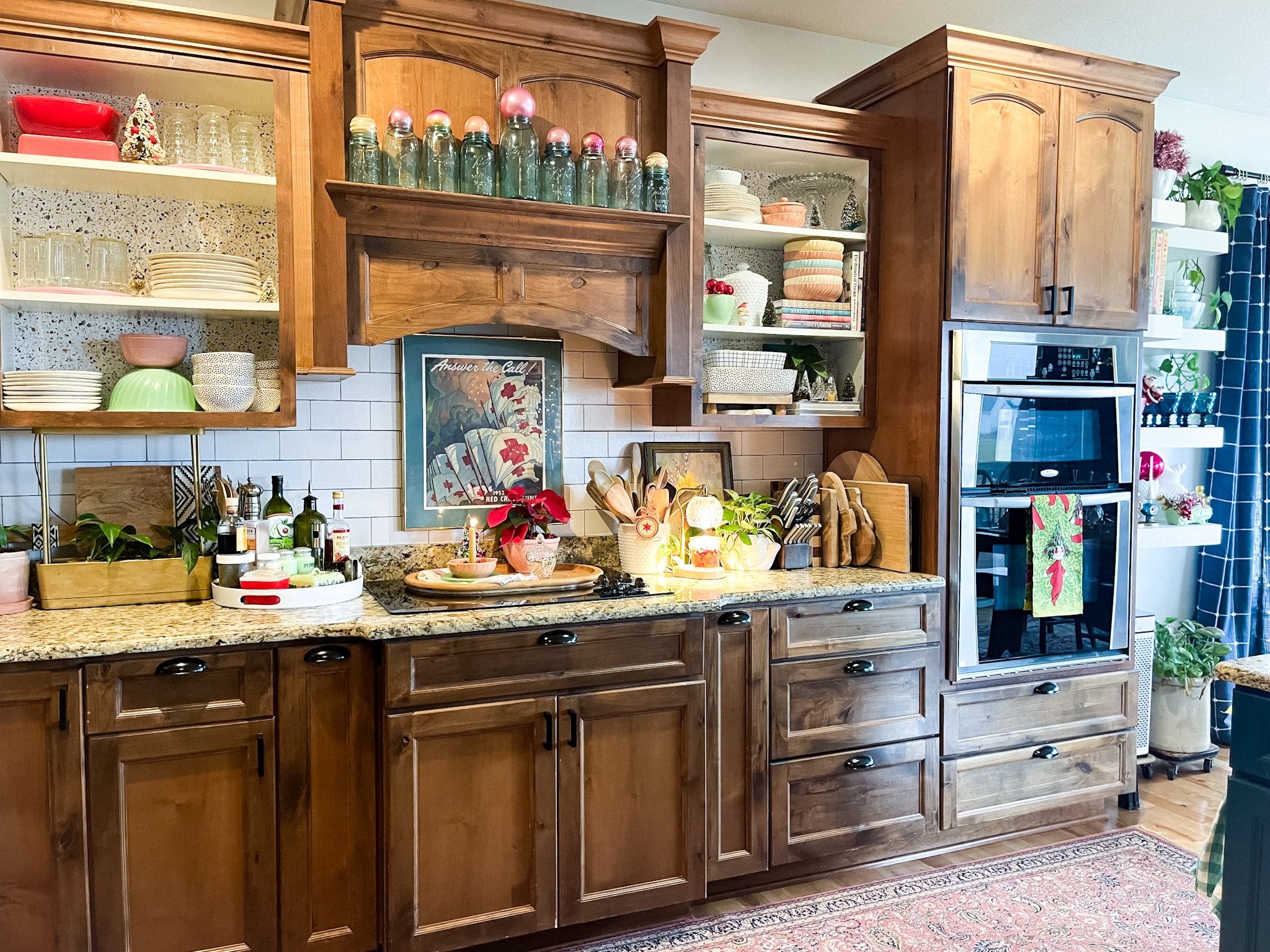kitchen with medium wood cabinets, a blue painted island, open shelving, and three globe pendant lights. Bits of vintage Christmas scattered throughout.