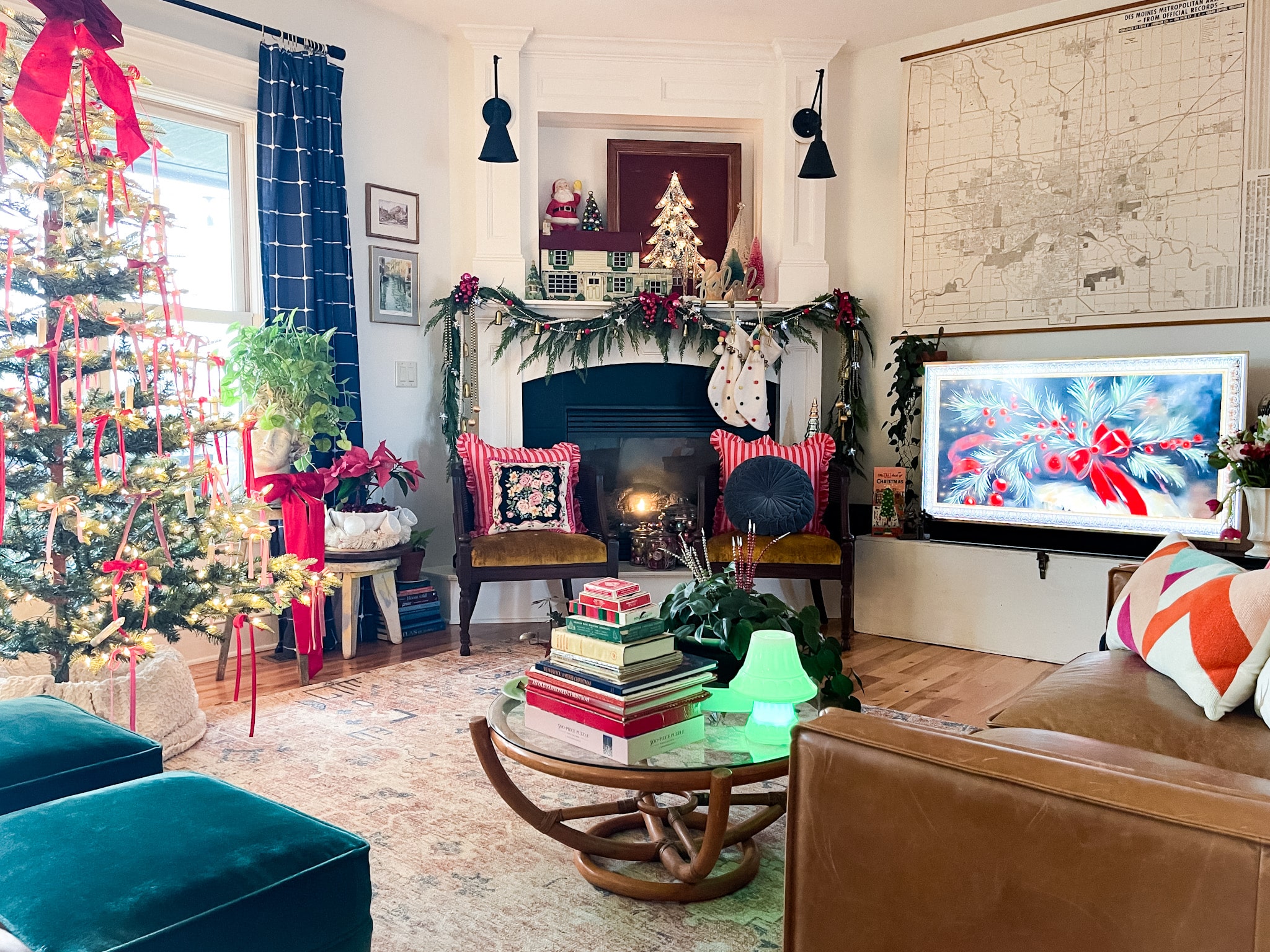 bamboo coffee table filled with vintage christmas decorations with a fireplace in the background and an art tv on. christmas tree decorated with red and pink ribbons, a leather couch, and two green footstools