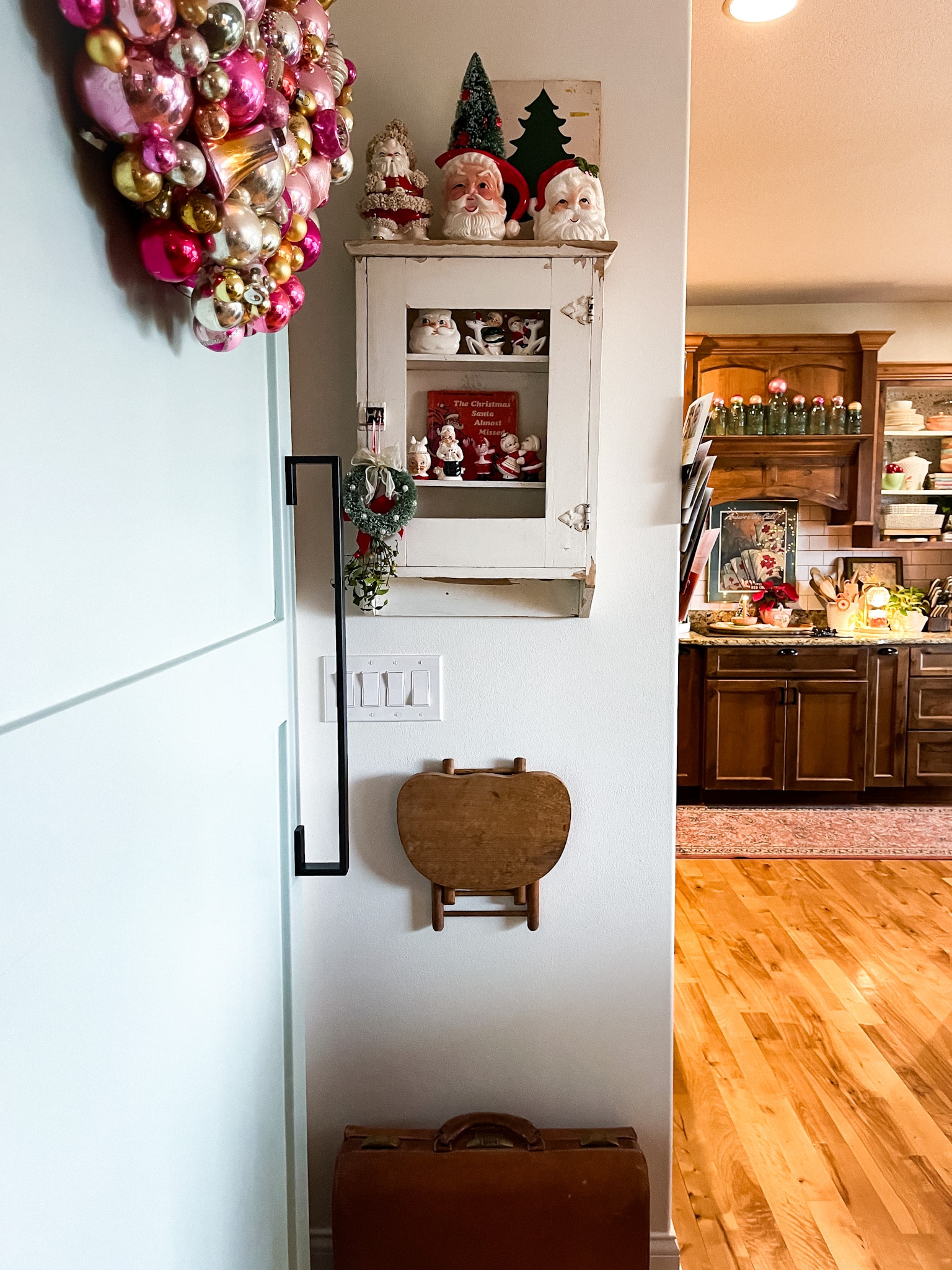antique medicine cabinet filled with vintage christmas decorations in front of a barn door with an ornament wreath on it