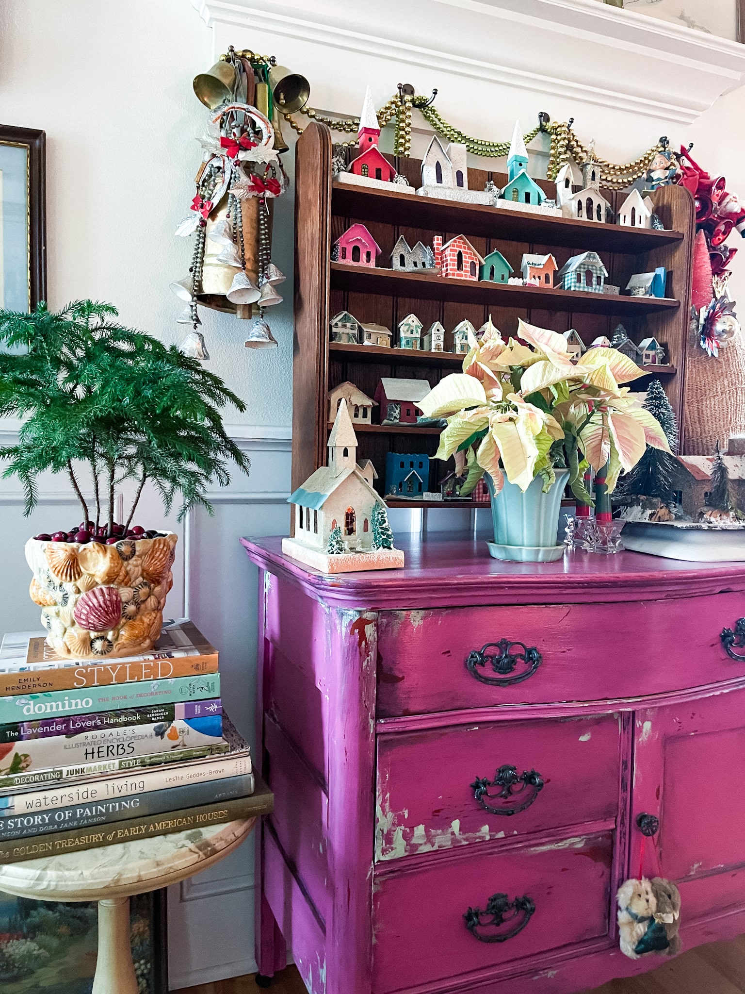 fuchsia commode decorated with vintage christmas decor, including putz houses, mercury glass garland, and plants