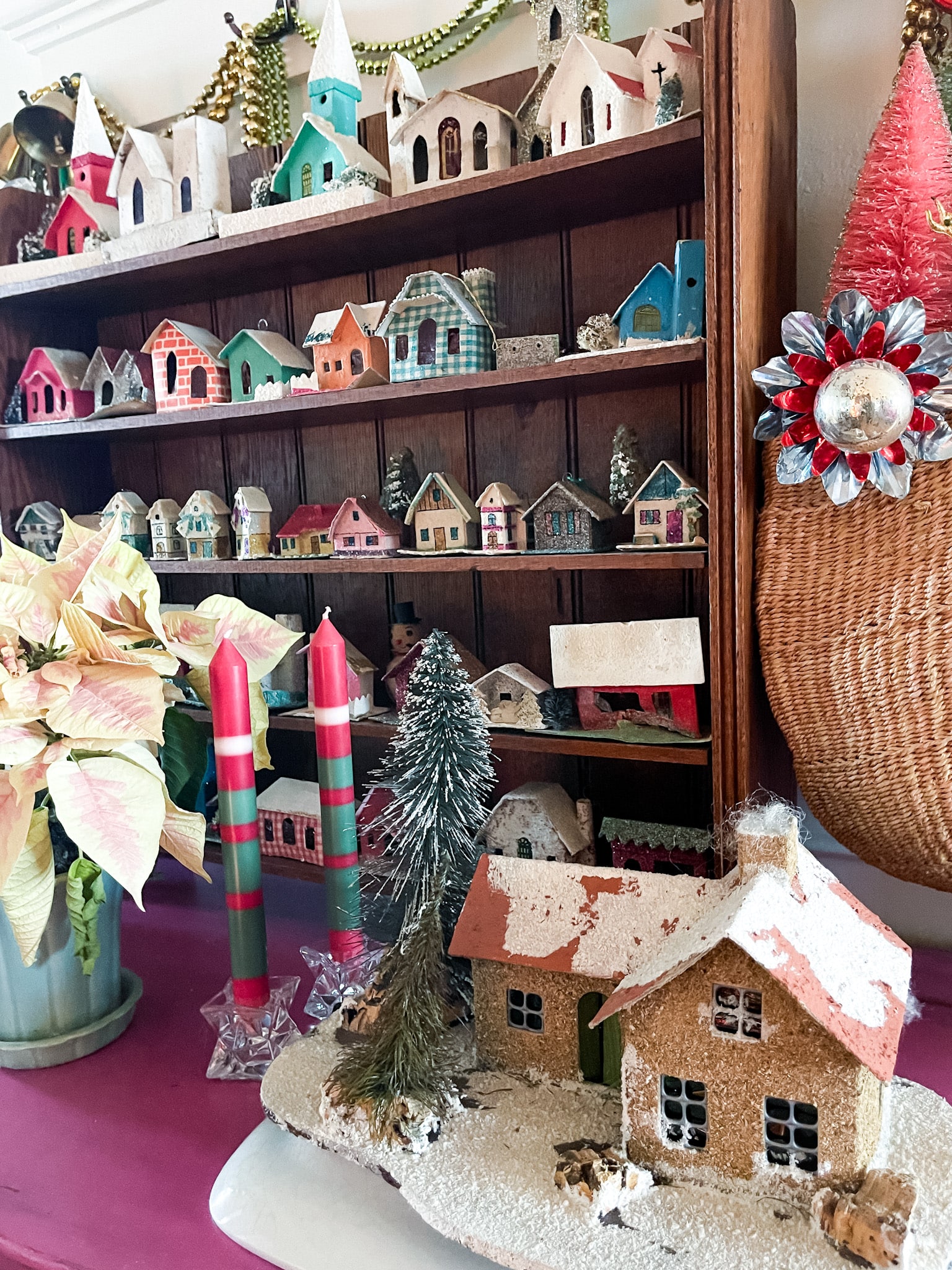 fuchsia commode decorated with vintage christmas decor, including putz houses, mercury glass garland, and plants