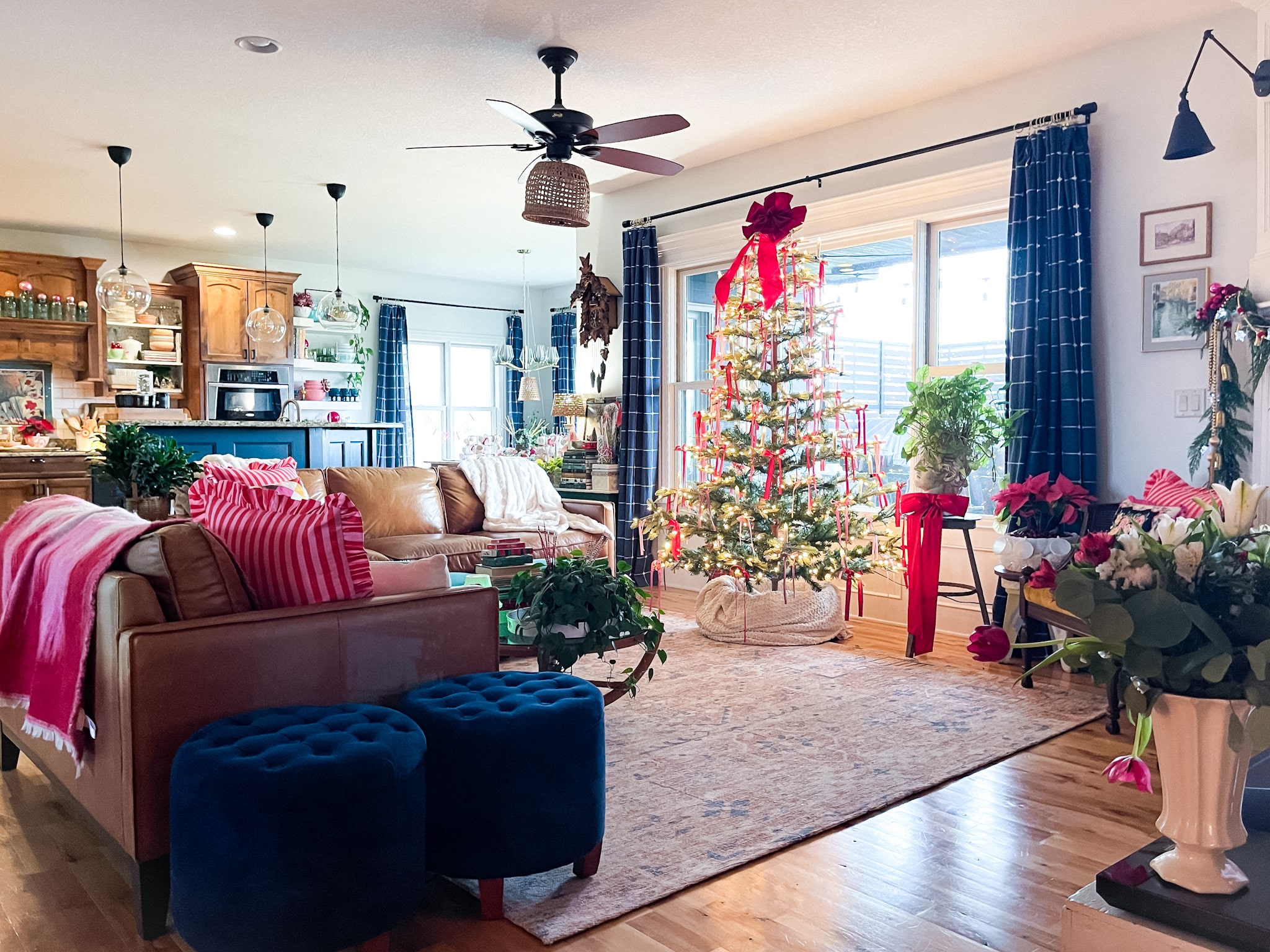 Living room filled with vintage christmas decor, two leather sofas, blue plaid curtains, and christmas tree filled with red and pink ribbons