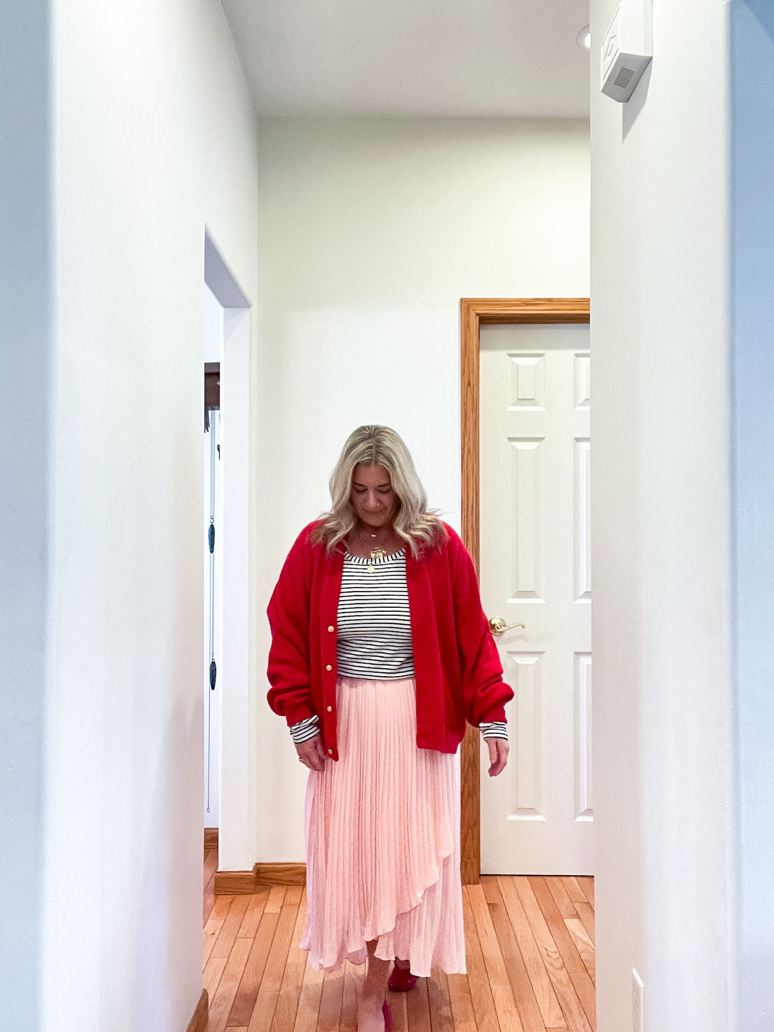 woman in a red sweater, black and white striped shirt, pink chiffon skirt, and red ballet flats