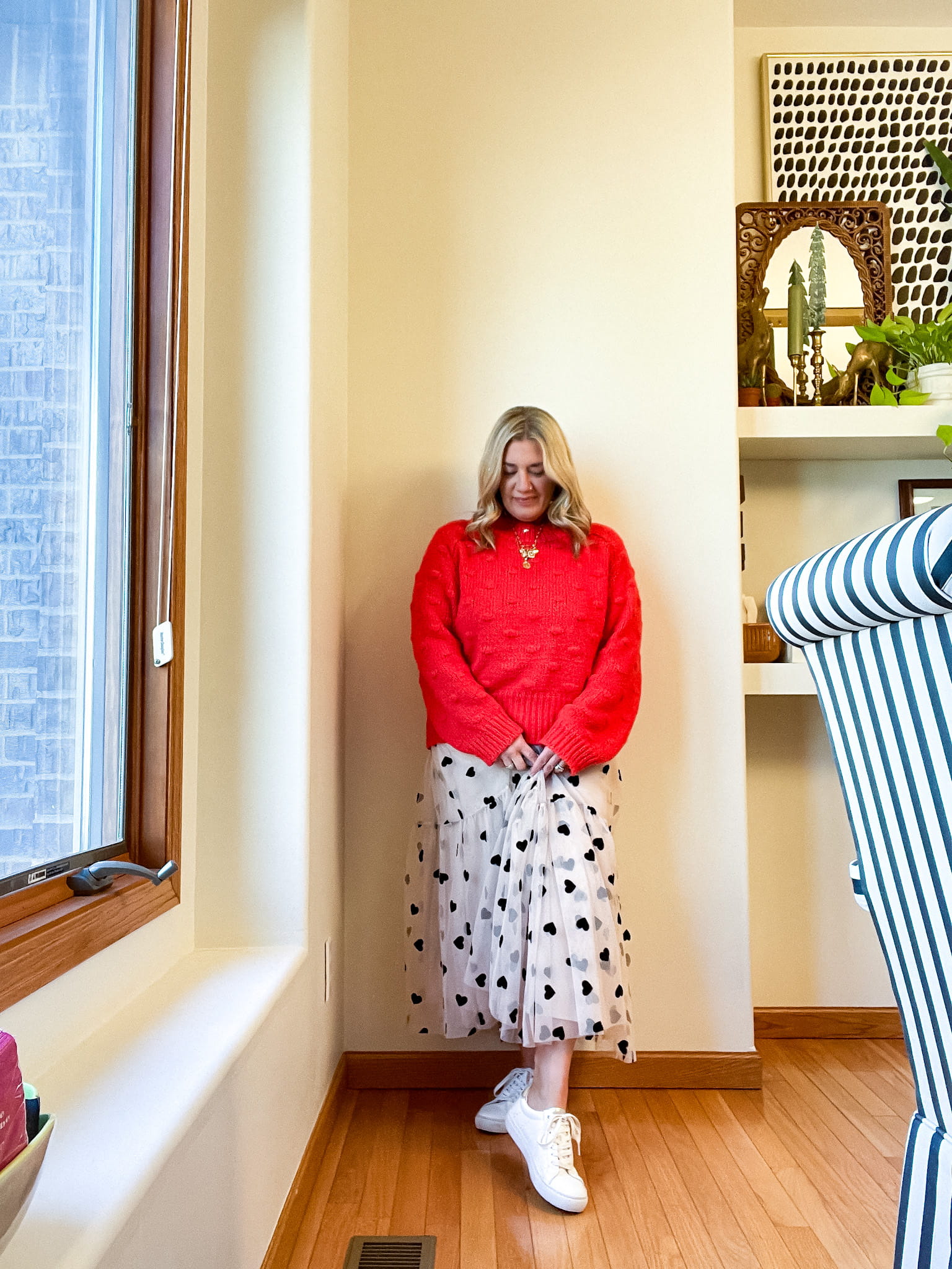 woman in a red puffed sweater, cream skirt with black hearts, and white tennis shoes