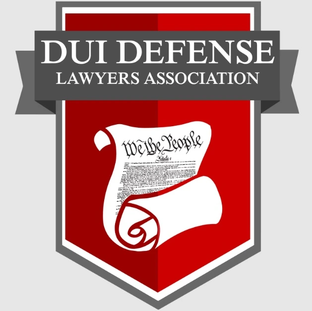 Logo for the DUI Defense Lawyers Association. It features a red shield with a white scroll of the US Constitution (We the People) on it, and a grey banner reading DUI DEFENSE LAWYERS ASSOCIATION.