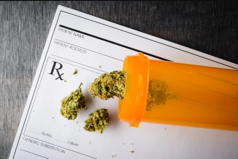 Cannabis flower buds spilling out of an orange prescription pill bottle onto a medical prescription pad (RX form)