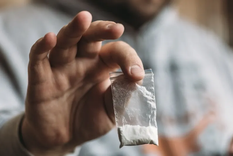 Close-up of a person's hand holding a very small clear plastic baggie containing a small amount of white powder, symbolizing illegal drug possession.