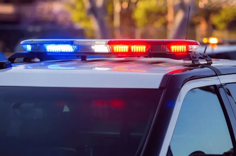 A close-up shot of the roof of a police vehicle showing the flashing red and blue LED light bar in action at dusk or night.