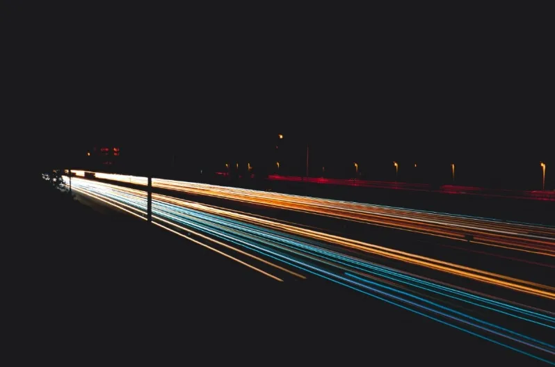 Long exposure photograph of orange (headlights) and blue/white (taillights) light trails from fast-moving vehicles on a dark highway at night.