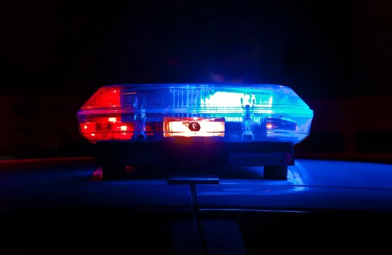 Close-up of a police car's red and blue emergency light bar flashing brightly on the roof against a dark night background.