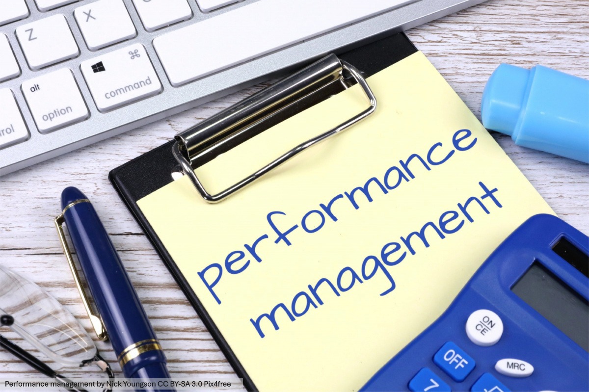 An image of a computer keyboard, calculator, and pen surrounding a clip board that says "performance management"