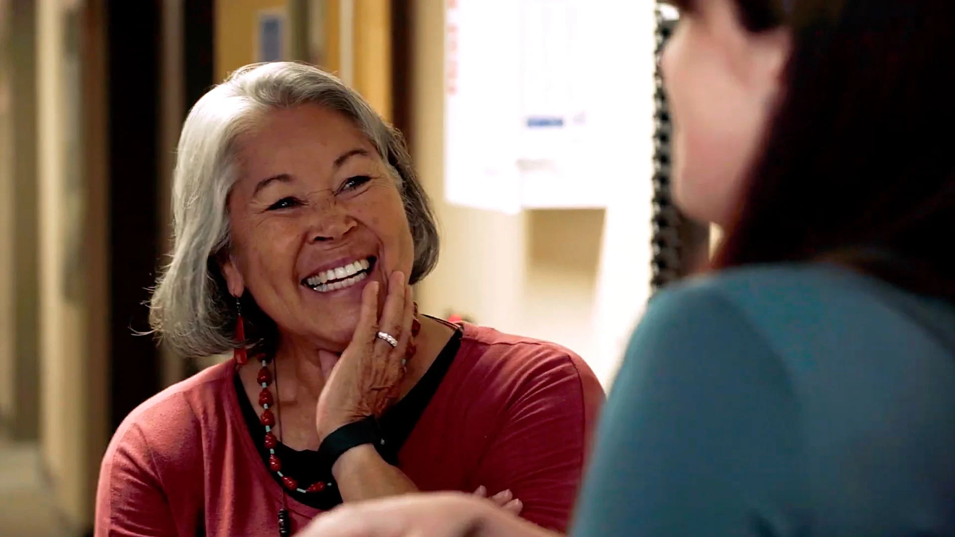 A woman in a hallway smiling and listening to a person talk
