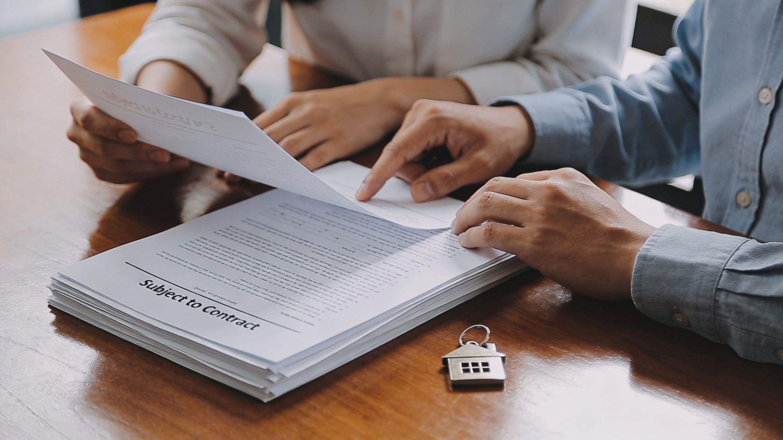 A real estate agent and a client reviewing a property contract with a house-shaped key on the table.