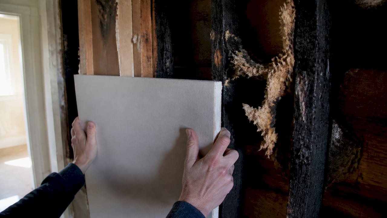 Hands fitting wooden studs in fire-damaged room