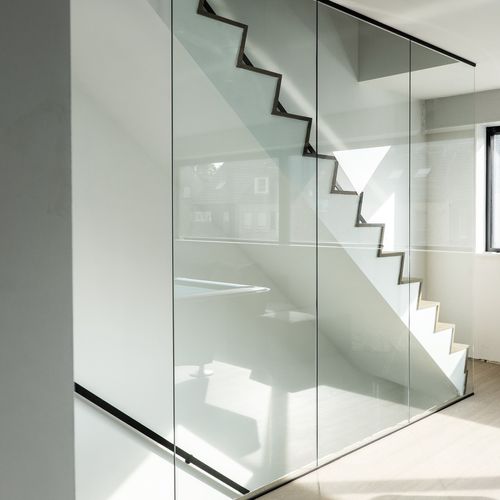 Plafondhoge glazen wand in helder glas met zwarte profielen aan trap