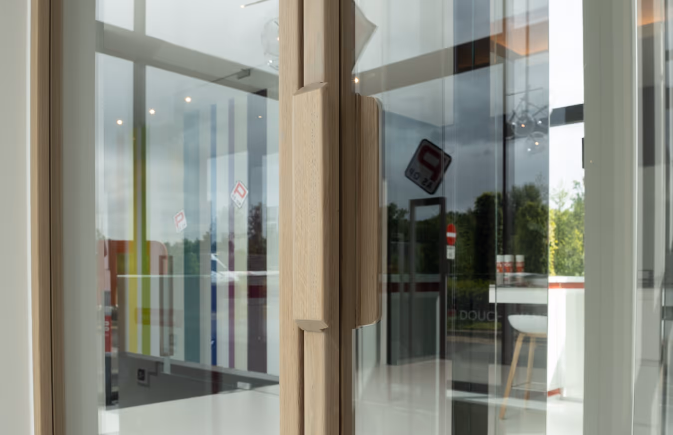 Close-up van een moderne houten deurklink van een glazen deur en weerspiegelingen van een binnenruimte.
