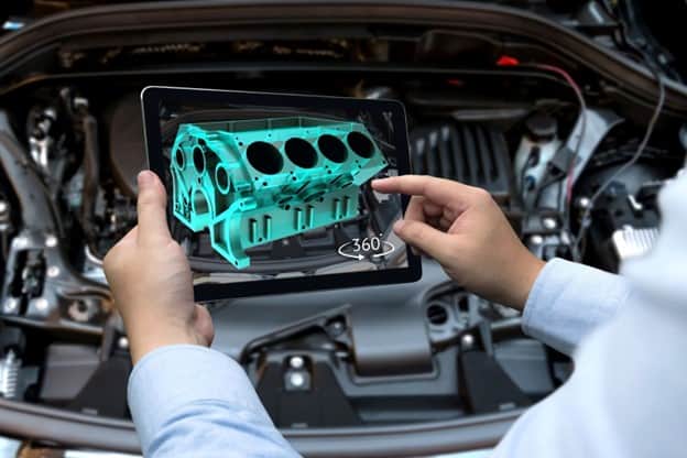 A tablet being held over a car engine showing a 3D rendered block on the screen