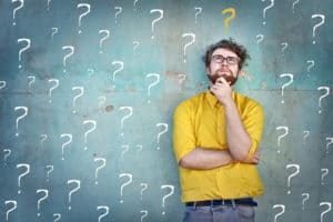 Man looking thoughtful in front of a blackboard filled with question marks