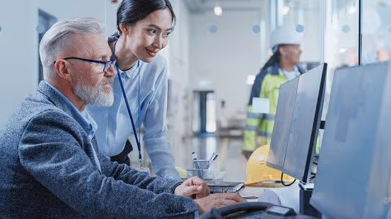 Factory Office Facility: Industrial Engineers Drafting Blueprints of a Heavy Industry Machine Parts on a Computer CAD Software. Asian Female Technician Discusses Work with Middle Aged Designer.