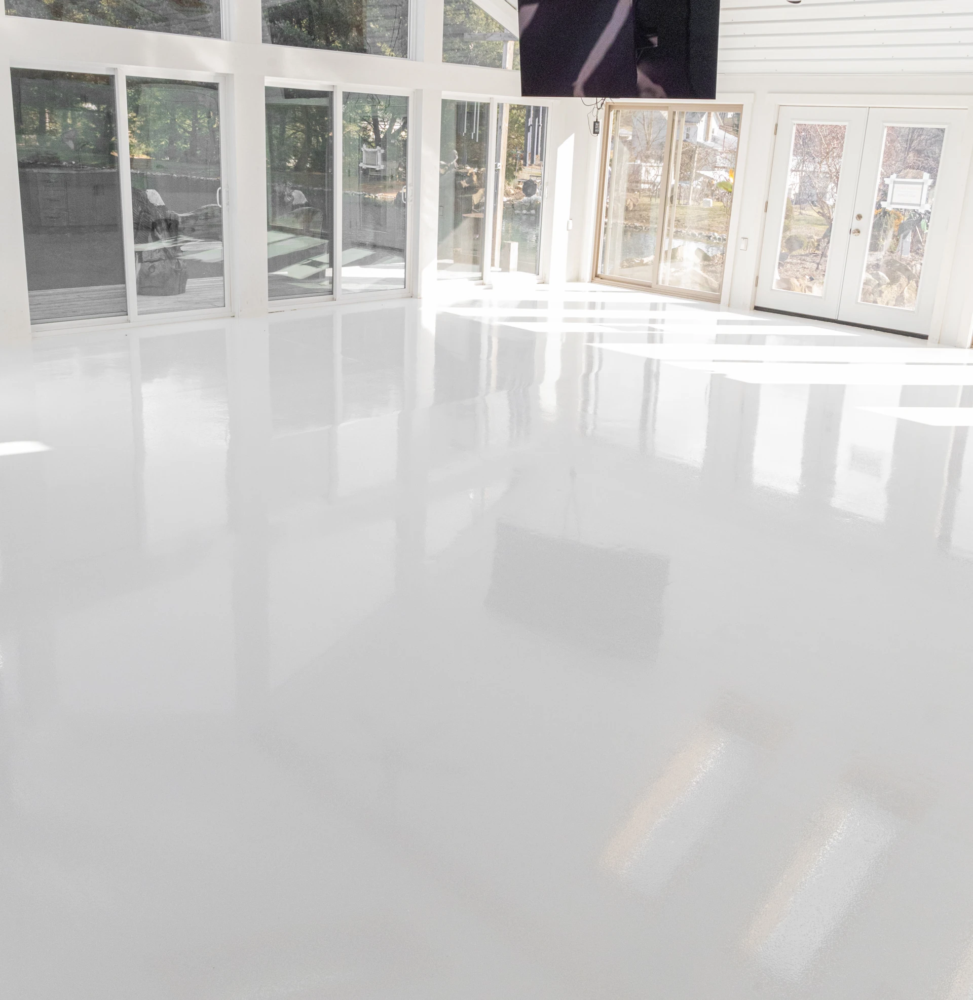 Wide view of a smooth, high-gloss solid epoxy garage floor reflecting natural light through large windows