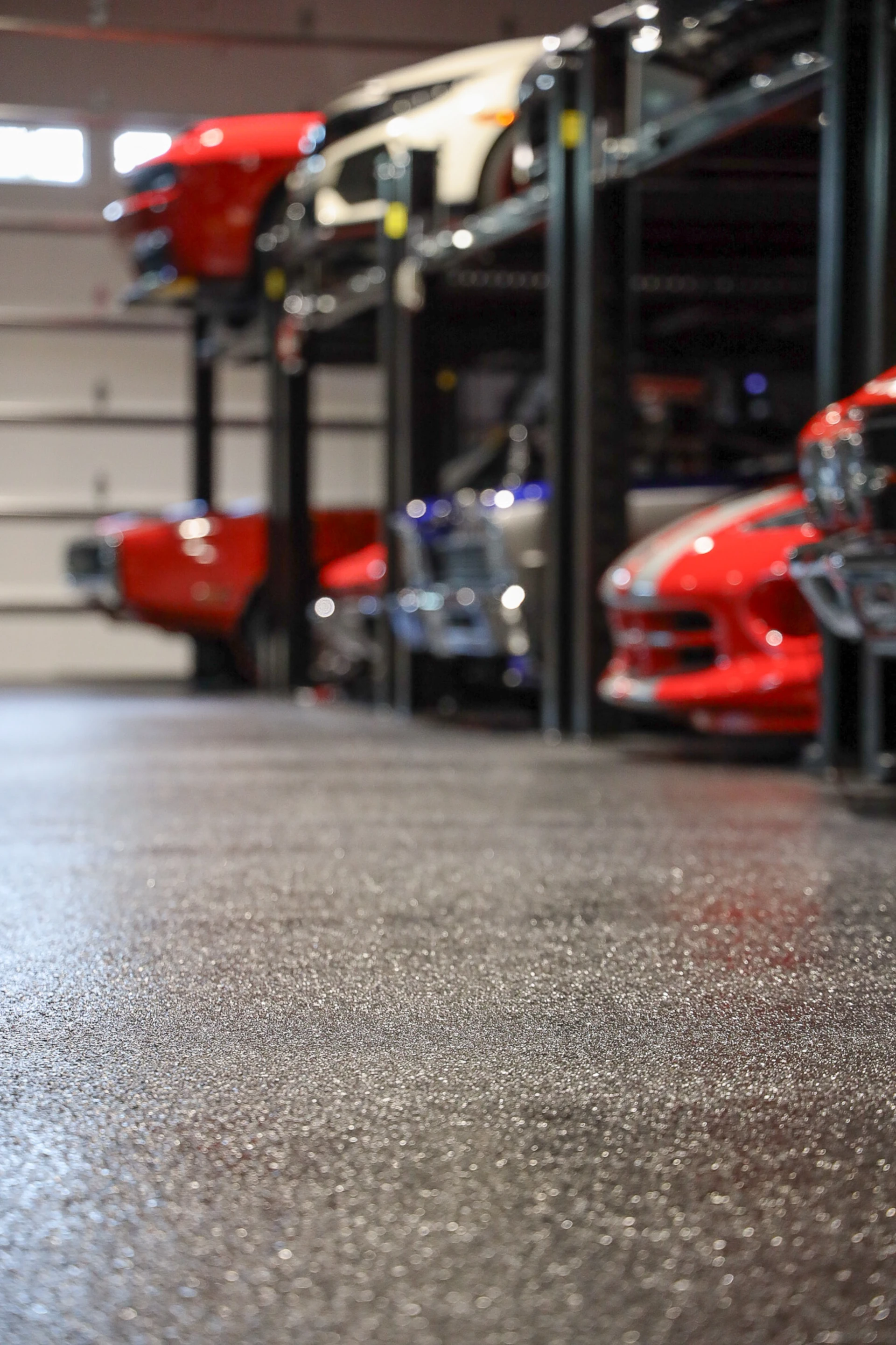 Close-up view of a textured decorative flake polyaspartic garage floor with classic cars in the background.